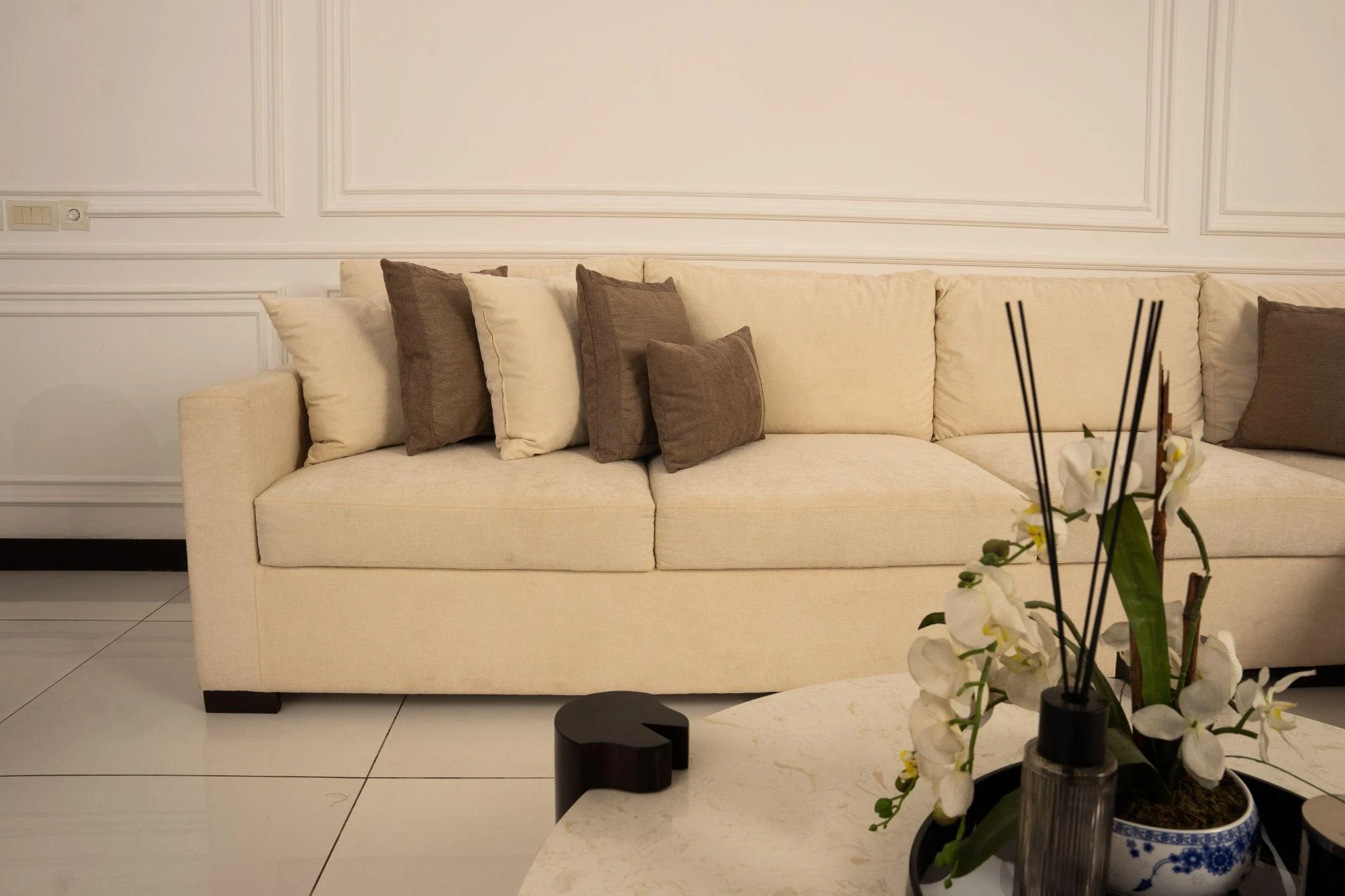 Close view of the cream sectional with taupe cushions and panelled wall.