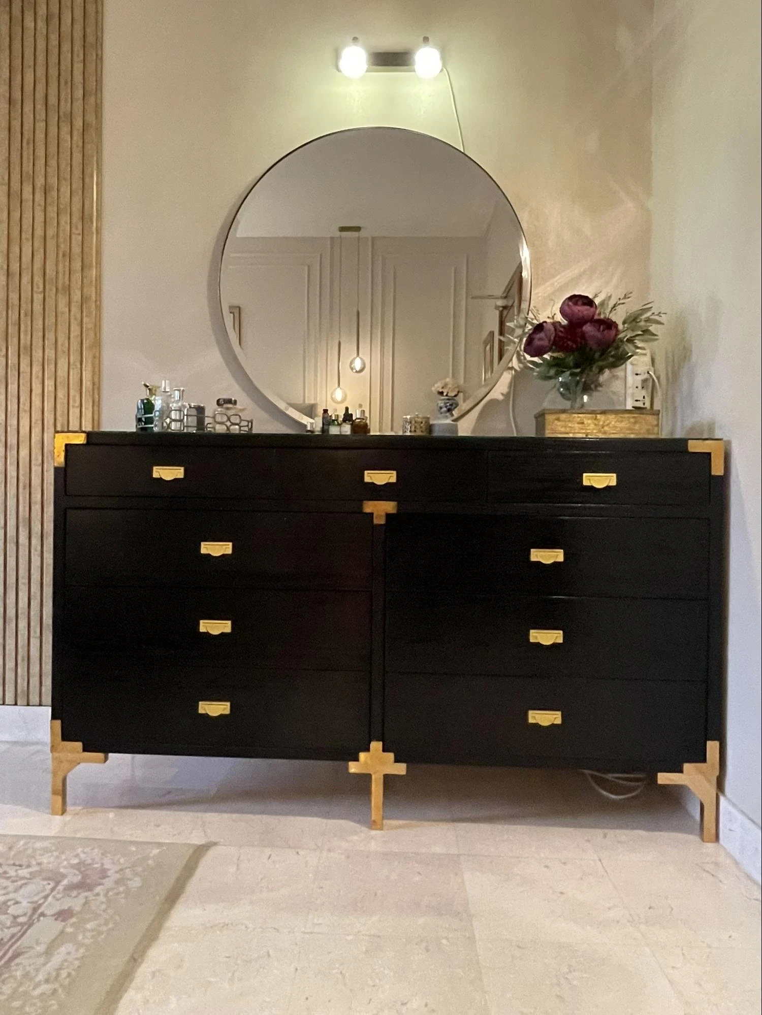 Black cabinet with a round mirror and gold hardware.